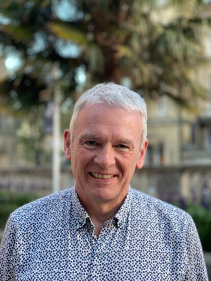 A colour portrait of me, a white man with grey hair. I'm smiling, and wearing a pale shirt with blue and brown dots on it.